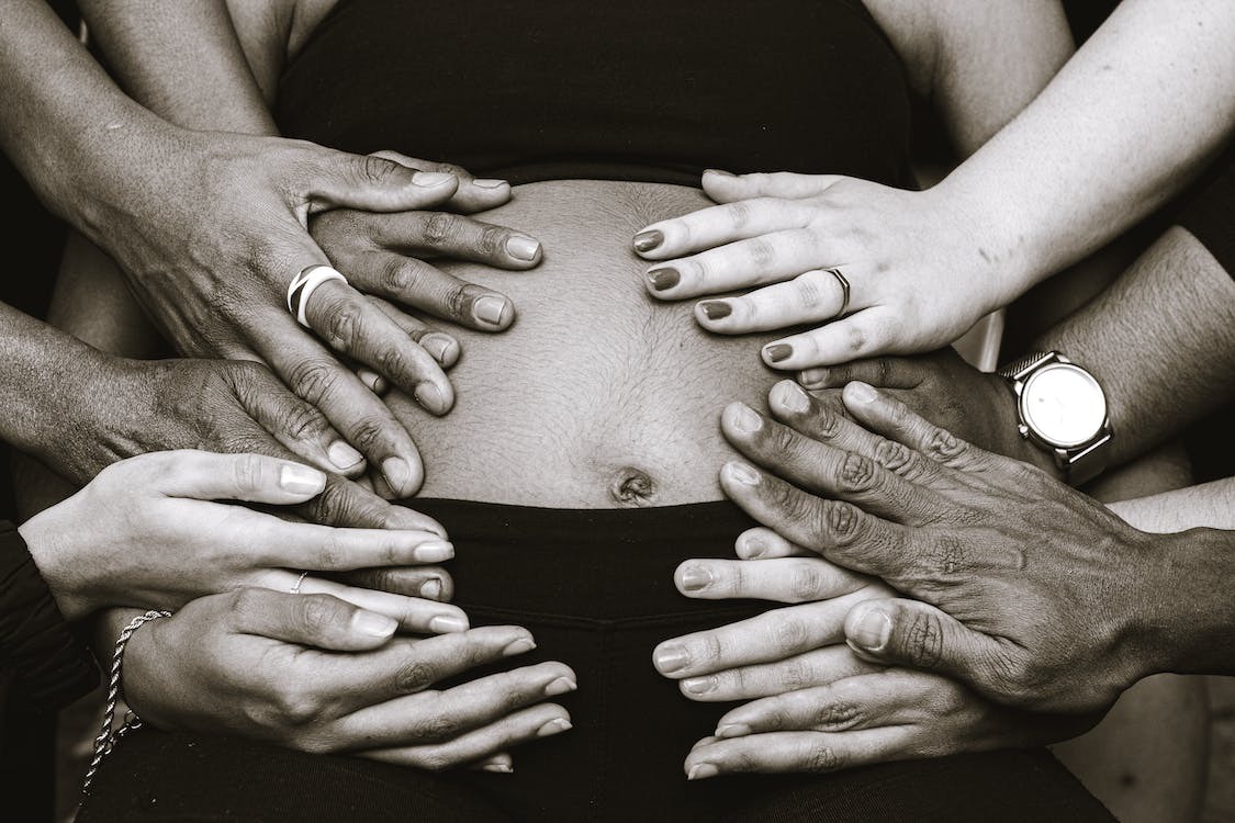 A photo of a pregnant belly with several hands touching it 