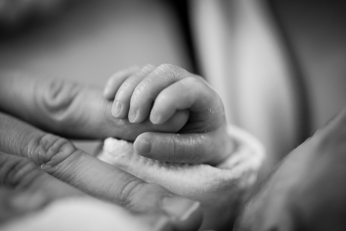 A black and white photo of a baby's hand holding someone's finger